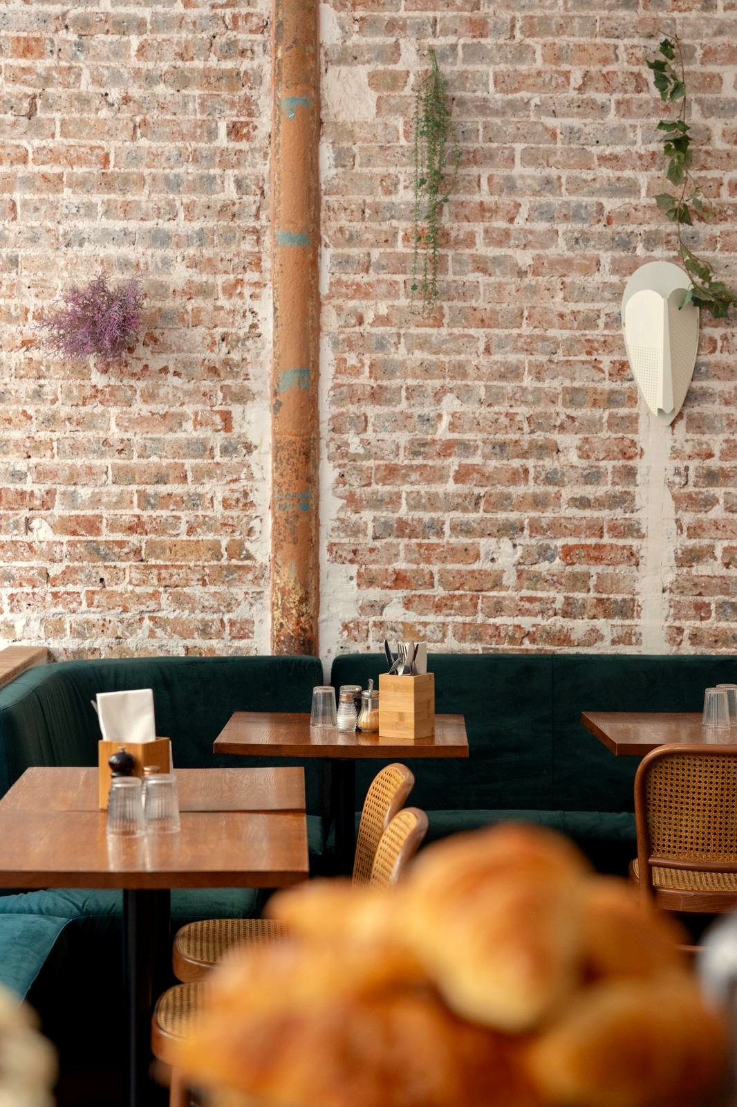 La salle de Papilles, banquette verte, tables en bois et mur de briques