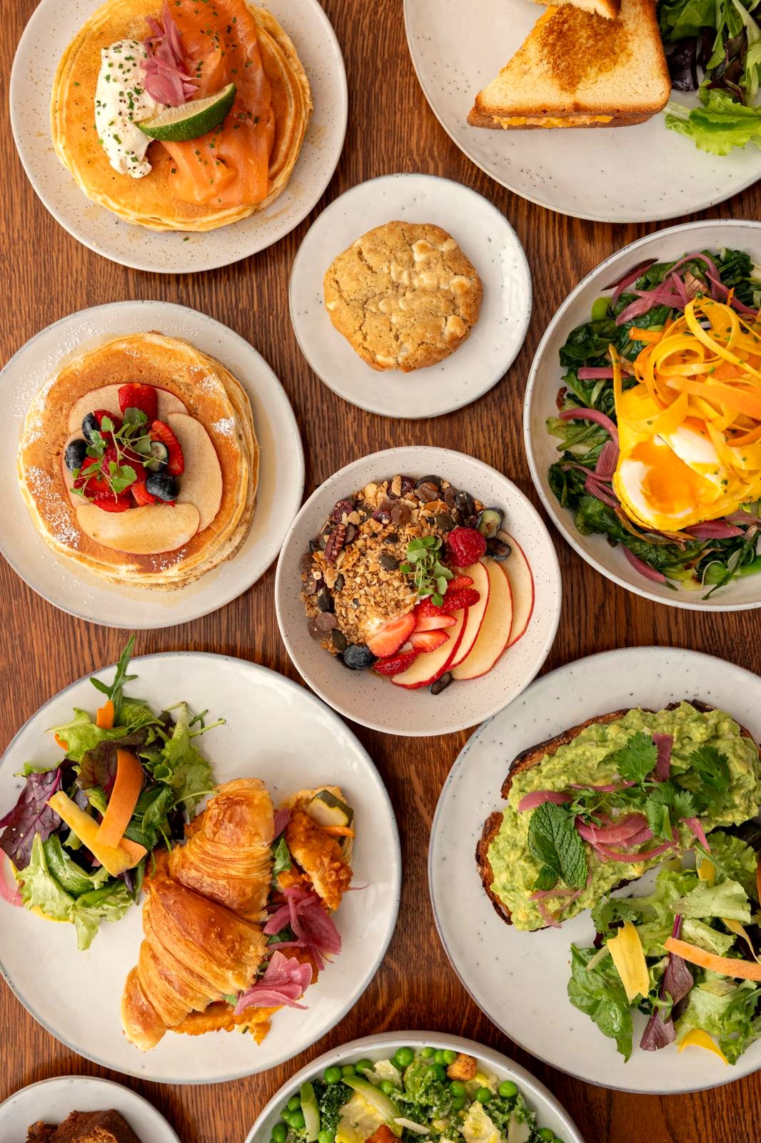 Table de brunch vue du dessus chez Papilles : pancakes, toast avocat, granola et salade